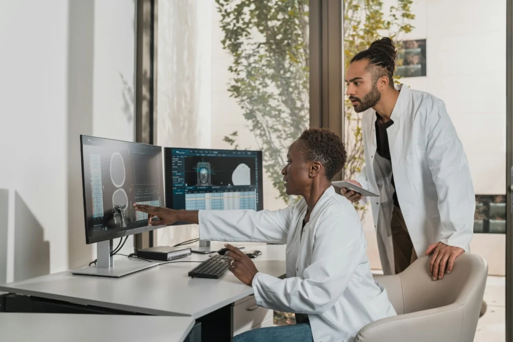 Two doctors in white lab coats review files on a computer.